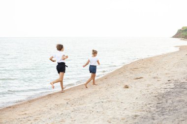 Çocuklar plaj boyunca koşar, deniz kenarında, güzel gün batımı, çocukların ayakları
