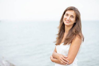 Sahilde beyaz elbiseli bir kız, güzel bir gün batımı, gülümsüyor.