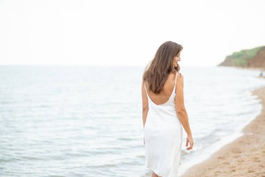 Sahilde beyaz elbiseli bir kız, güzel bir gün batımı, gülümsüyor.