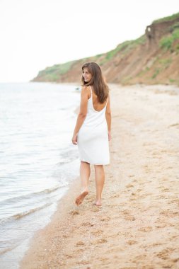 Sahilde beyaz elbiseli bir kız, güzel bir gün batımı, gülümsüyor.