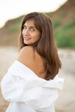 Deniz kenarındaki plajda mayo ve beyaz gömlekli bir kız, güzel bir gün batımı, gülümsüyor.