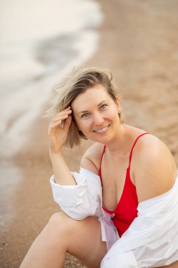 Deniz kenarındaki plajda mayo ve beyaz gömlekli bir kız, güzel bir gün batımı, gülümsüyor.