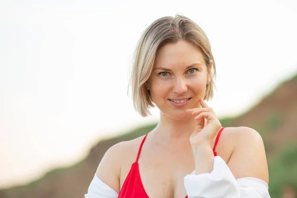 Deniz kenarındaki plajda mayo ve beyaz gömlekli bir kız, güzel bir gün batımı, gülümsüyor.