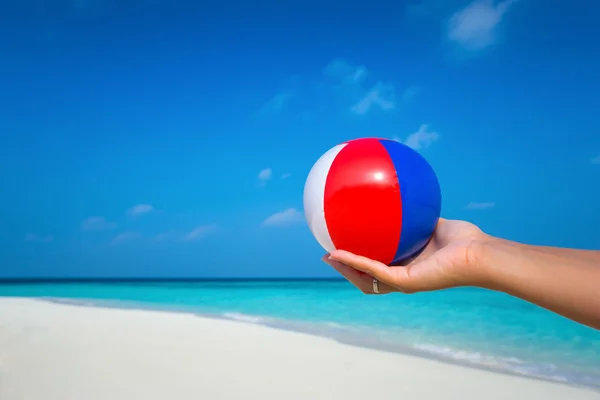 Mão feminina segurando uma bola em uma bela praia com um turquesa — Fotografia de Stock