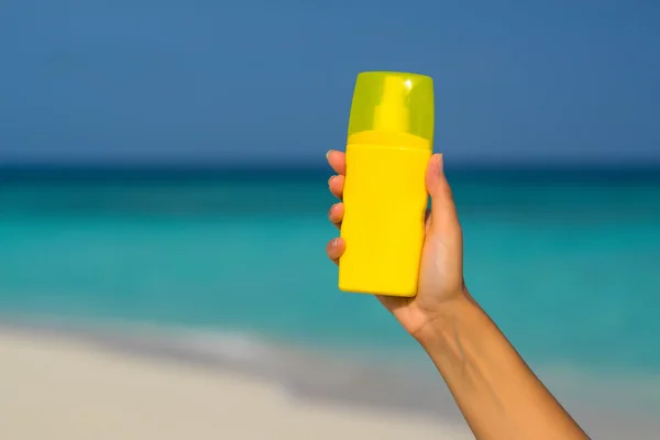 Zonnebrand crème fles in de hand op tropisch strand — Stockfoto