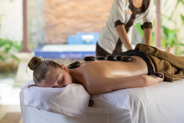 Mujer joven recibiendo masaje de piedra caliente en el salón de spa. Belleza tratar — Foto de Stock