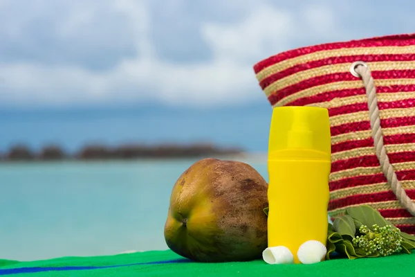 Sunscreen, bag and coconut on tropical beach — Stock Photo, Image