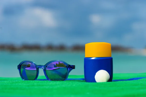 Zonnebrandcrème, handdoek en zonnebril op tropisch strand — Stockfoto