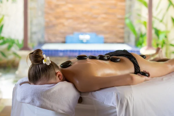 Mujer joven recibiendo masaje de piedra caliente en el salón de spa. Belleza tratar — Foto de Stock