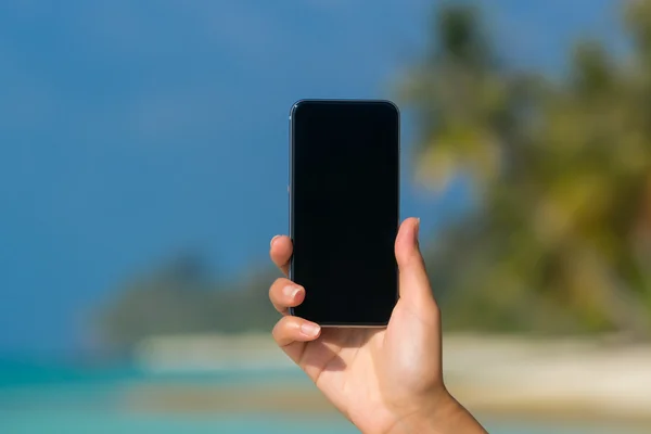 Vrouw hand tonen een lege slimme telefoon op het strand met de zee — Stockfoto