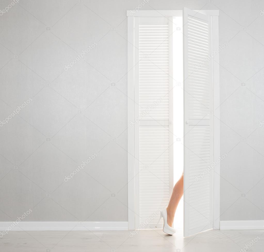 Women leg in white shoe looks out of the open door