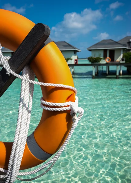 Half of orange lifebuoy in foreground on sea and bungalows backg — Stock Photo, Image