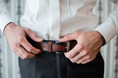 Erkek aksesuarları. Adam kahverengi bir deri kemer takıyor. Erkek elleri yakın.