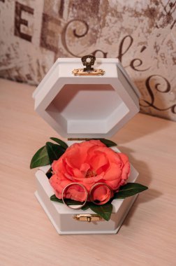 Beyaz bir kutuda, turuncu bir gülün üzerinde altın yüzükler.
