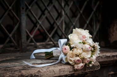 Kahverengi arkaplanda beyaz ve pembe güller olan gelin buketi. Metal ızgaradan bir arka planda gelin buketi