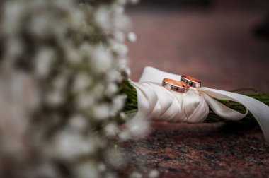 Beyaz çiçekli çiçek aranjmanı, bir kurdeleli düğün buketi ve bir taşın üzerinde duran iki altın yüzük. Düğün dekorasyonu, sanat eseri, çiçekçi.