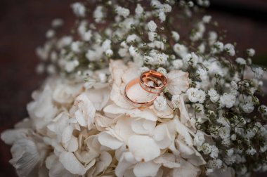 Beyaz çiçekli çiçek aranjmanı, bir kurdeleli düğün buketi ve bir taşın üzerinde duran iki altın yüzük. Düğün dekorasyonu, sanat eseri, çiçekçi.