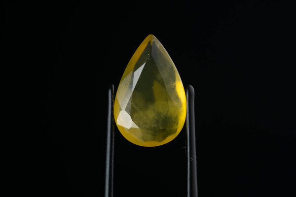 Yellow opal in tweezers on a black background