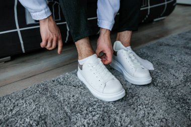 Adam beyaz spor ayakkabıların bağcıklarını bağlıyor. Damat güzel ayakkabılar giyer ve bağcıklarını bağlar..