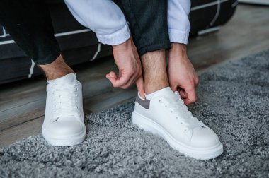Adam beyaz spor ayakkabıların bağcıklarını bağlıyor. Damat güzel ayakkabılar giyer ve bağcıklarını bağlar..