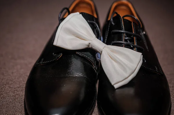 White bow tie on black classic shoes on brown background