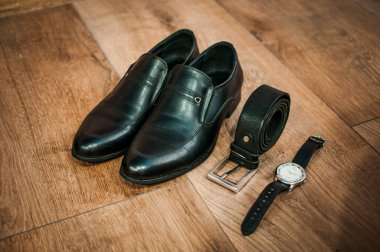 Siyah deri erkek ayakkabıları, yerde bir saat ve kemer var. Damat aksesuarları
