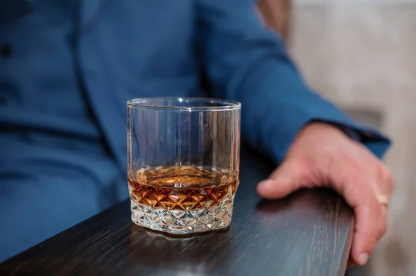 A glass of whiskey on a wooden stand, a man sits in the background