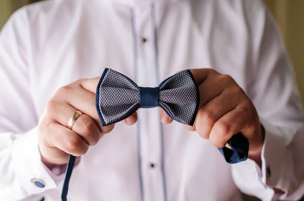Blue bow tie in the hands of the groom. Bow tie in the hands of a man