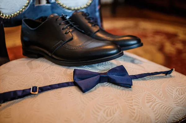Accessories for the groom. Black leather shoes, gold wedding rings, blue bow tie, perfume