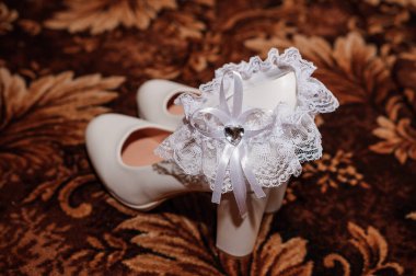 Beyaz kadın ayakkabıları ve kahverengi arka planda gelinin jartiyeri. Gelin için düğün aksesuarları