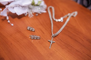 Küpeler, altın bir yüzük ve kahverengi arka planda haçlı gümüş bir zincir.