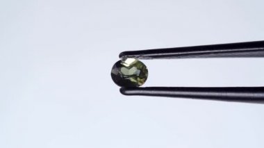 Doğal yeşil kornerupin mücevheri sehpanın üzerinde cımbızla