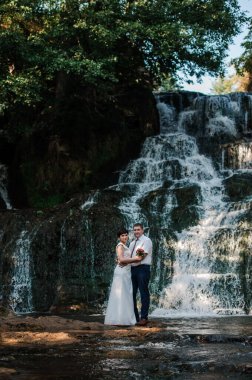 Gelin ve damat bir şelalenin arka planında dururlar.