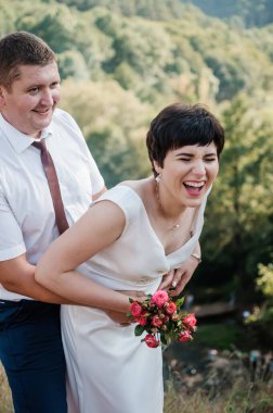 Yeni evliler ormanın arka planında sarılıp öpüşürler.