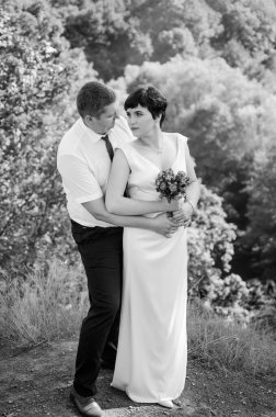 Yeni evliler ormanın arka planında sarılıp öpüşürler.