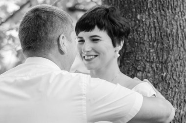 Yeni evliler ormanın arka planında sarılıp öpüşürler.