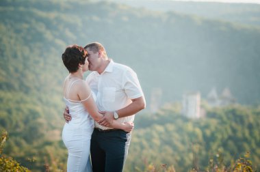 Yeni evliler ormanın arka planında sarılıp öpüşürler.