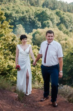 Yeni evliler ormanın arka planında el ele tutuşuyorlar. Bir kadının elini tutan bir erkek.