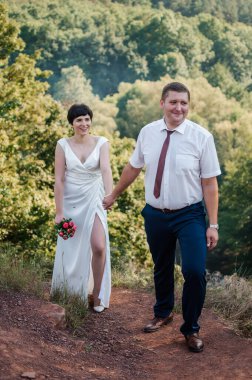 Yeni evliler ormanın arka planında el ele tutuşuyorlar. Bir kadının elini tutan bir erkek.