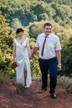 Yeni evliler ormanın arka planında el ele tutuşuyorlar. Bir kadının elini tutan bir erkek.