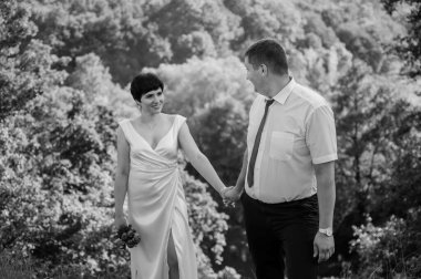 Yeni evliler ormanın arka planında el ele tutuşuyorlar. Bir kadının elini tutan bir erkek.