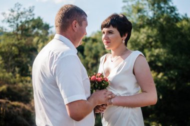 Yeni evliler ormanın arka planında el ele tutuşuyorlar. Bir kadının elini tutan bir erkek.