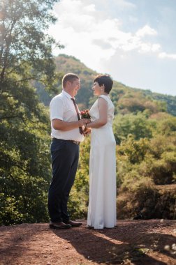 Yeni evliler ormanın arka planında el ele tutuşuyorlar. Bir kadının elini tutan bir erkek.