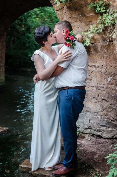 Recém Casados Abraçar Beijar Contra Fundo Água Arco Pedra — Fotografia de Stock