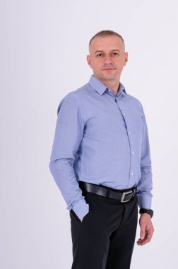 Mavi gömlekli ve siyah pantolonlu bir adam beyaz arka planda duruyor.