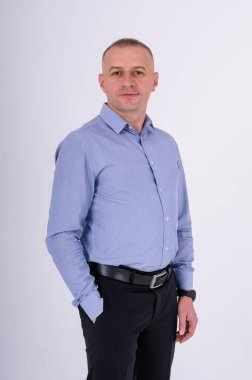 Mavi gömlekli ve siyah pantolonlu bir adam beyaz arka planda duruyor.