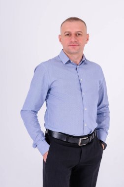 Mavi gömlekli ve siyah pantolonlu bir adam beyaz arka planda duruyor.