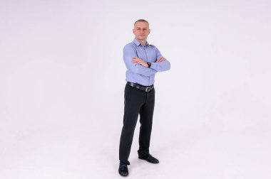 Mavi gömlekli ve siyah pantolonlu bir adam beyaz arka planda duruyor.