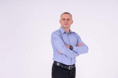 Mavi gömlekli ve siyah pantolonlu bir adam beyaz arka planda duruyor.