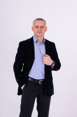 Mavi gömlekli, siyah pantolonlu ve beyaz arka planda mavi ceketli bir adam.